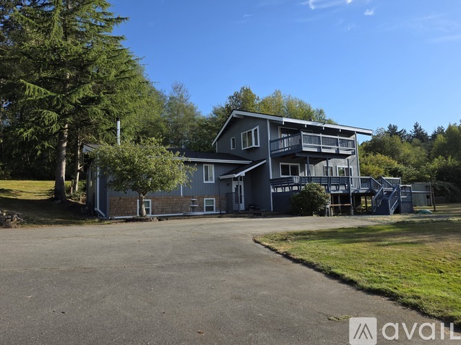 A large house with a balcony is surrounded by trees and has a driveway in front.