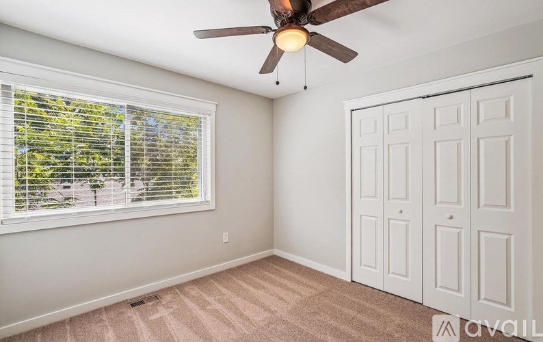 A room with a ceiling fan, a window with blinds, and a carpeted floor.