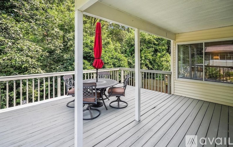 A red umbrella is on a white railing on a wooden deck.