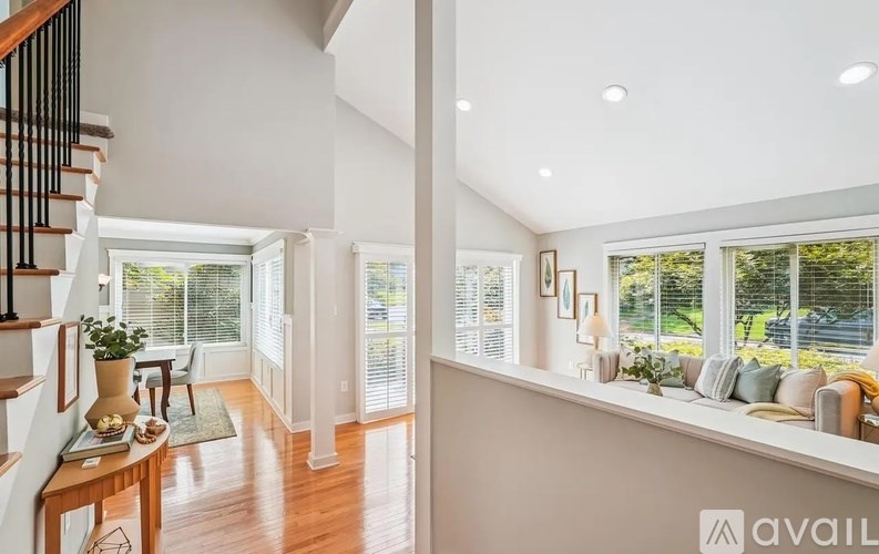 A well-lit, spacious living room with a staircase on the left and a row of windows on the right.