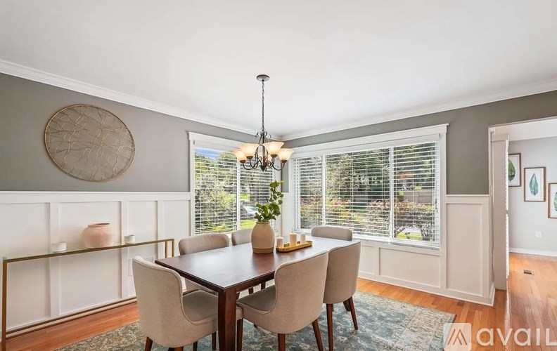 A dining room with a wooden table and chairs, a chandelier, and a window with blinds.