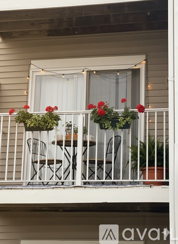 A balcony with a table and chairs is decorated with red flowers.