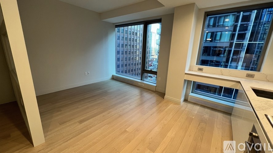 A spacious room with wooden flooring and large windows overlooking a cityscape.