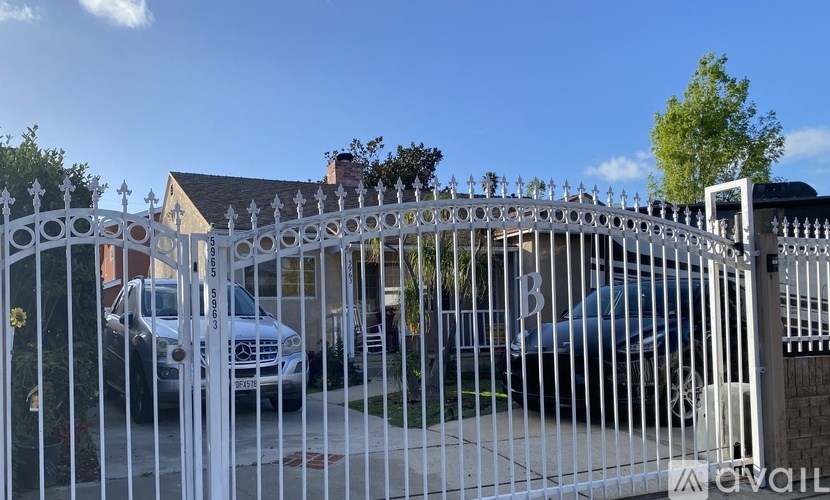 A white car is parked in front of a house with a white fence.
