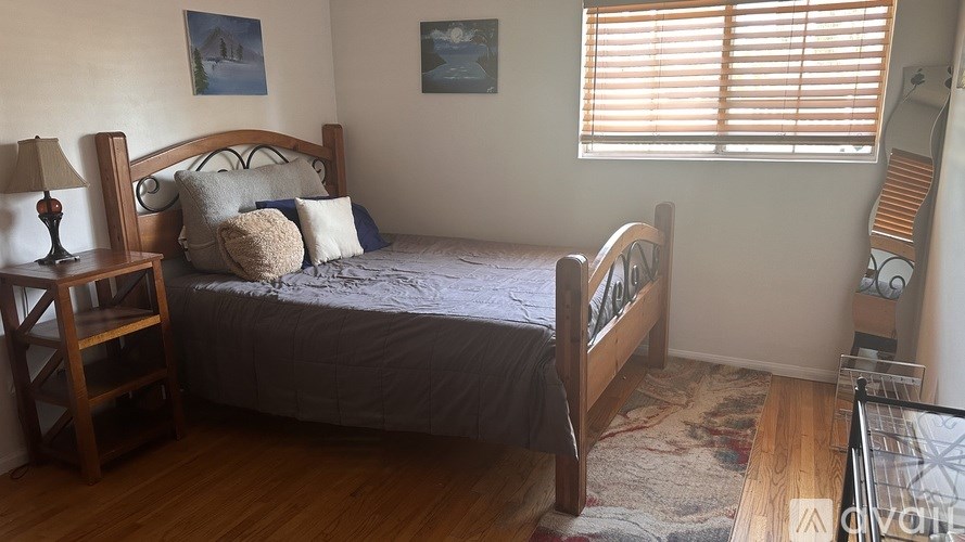 A bedroom with a bed, a nightstand, a lamp, and a window with blinds.