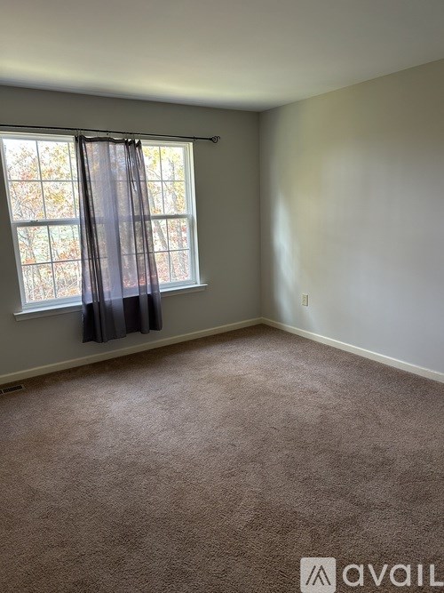 A room with a carpeted floor and a window with curtains.