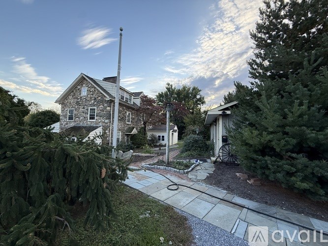 A house with a stone exterior is surrounded by greenery and a gravel pathway.