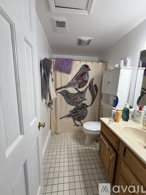 A bathroom with a white door, a white toilet, a white sink, and a shower curtain with a bird design.
