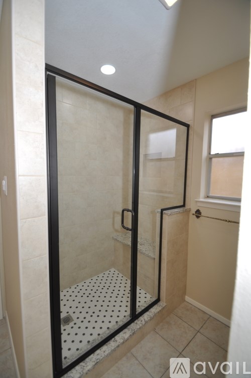 A glass shower stall with a black frame and a white tiled floor.