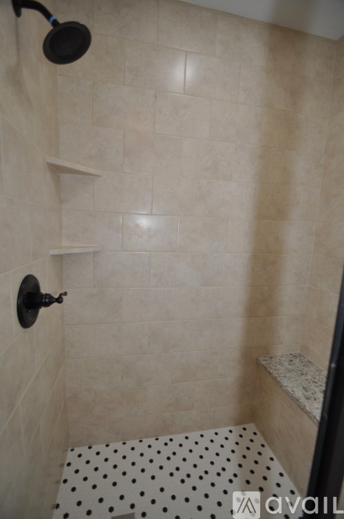 A shower with a black shower head and a tiled floor with a black and white tile.