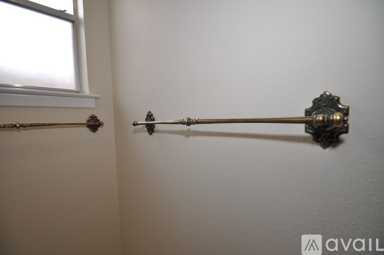 A long, ornate, brass curtain rod with a finial is mounted on a white wall.