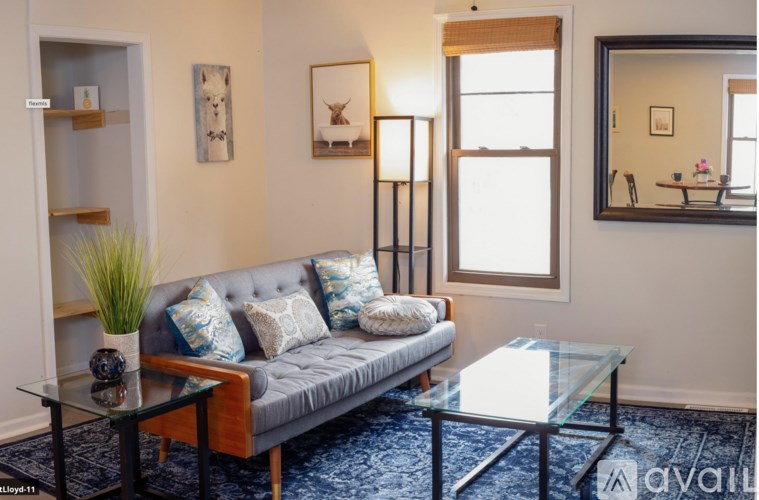 A living room with a grey couch, a glass table, and a mirror on the wall.