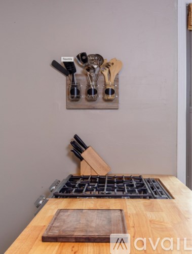 A set of utensils is displayed on a wall rack above a wooden cutting board.