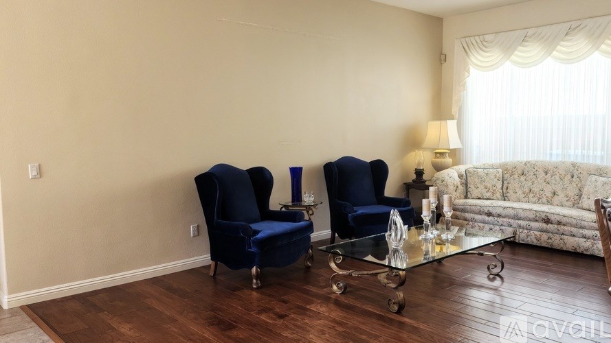 A living room with two blue chairs and a glass coffee table.