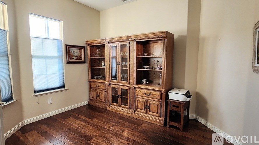 A wooden cabinet with glass doors is in the corner of a room with hardwood floors.