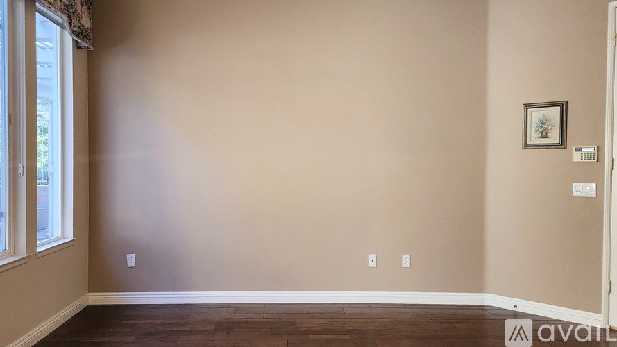A room with beige walls and a wooden floor with a window on the left side.