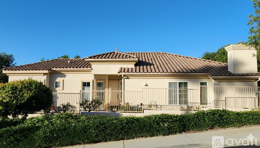 A house with a brown roof and a white fence is for sale.