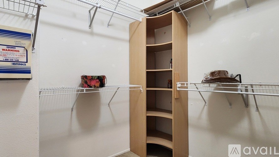 A wooden shelf unit is open in a room with a white wall and a wire shelf with a hat and a bag on it.