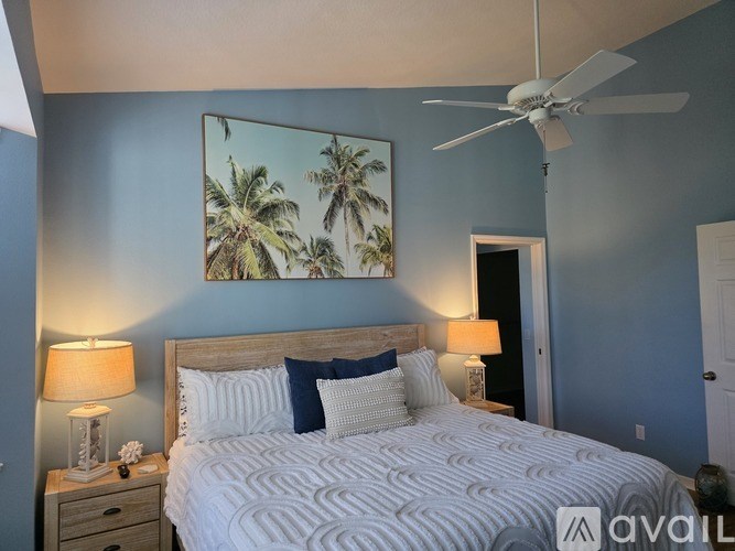 A bedroom with a bed, a ceiling fan, and a painting of palm trees on the wall.