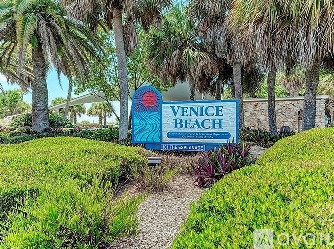A sign for Venice Beach is displayed in front of some greenery.