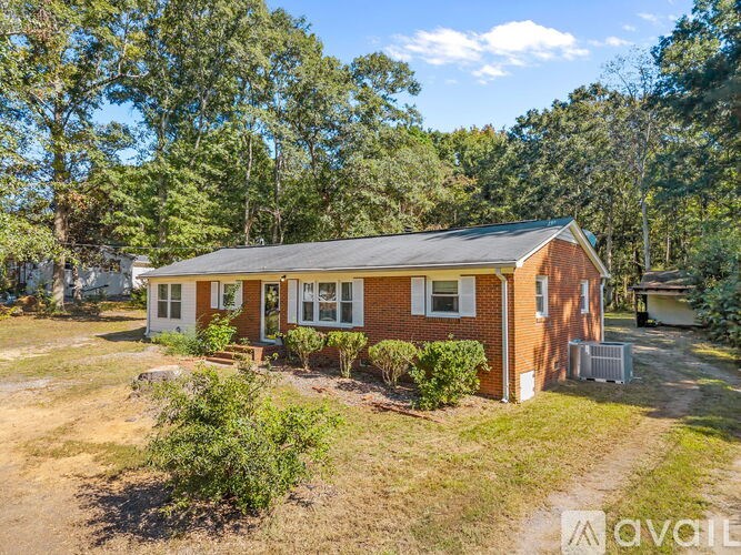 A house with a brown roof and white windows is surrounded by greenery.