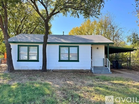 A white house with a green roof and a tree in front.
