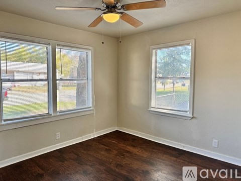 A room with a ceiling fan and two windows.