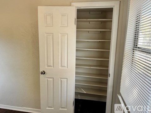 A white door with a handle is open to a room with a window and blinds.