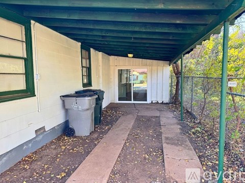 A long covered walkway with a trash can on the left and a fence on the right.