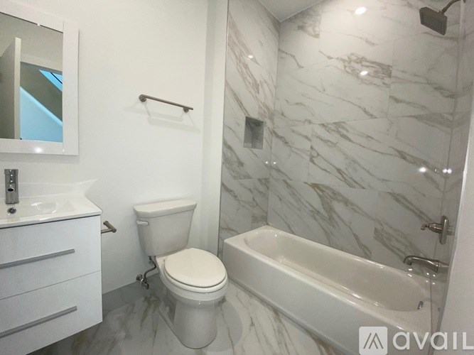 A white toilet sits in a marble bathroom next to a bathtub.