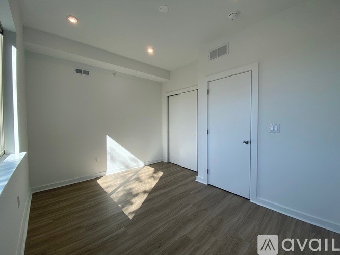 A room with wooden flooring and white walls, with a door on the right and a window on the left.