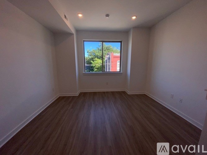 A room with wooden floors and a window showing a red building outside.