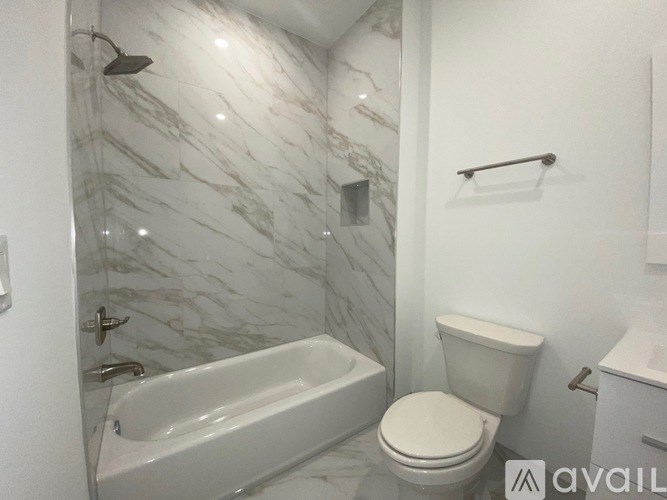 A white toilet sits next to a bathtub in a bathroom with marble walls.