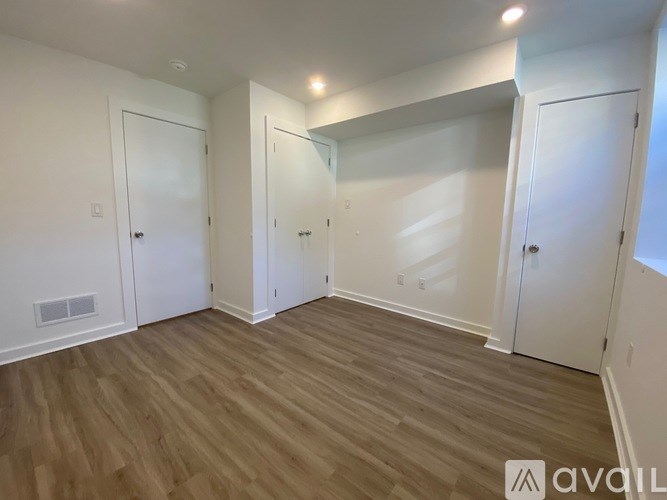 A room with white walls and wooden flooring, with four doors and a window.