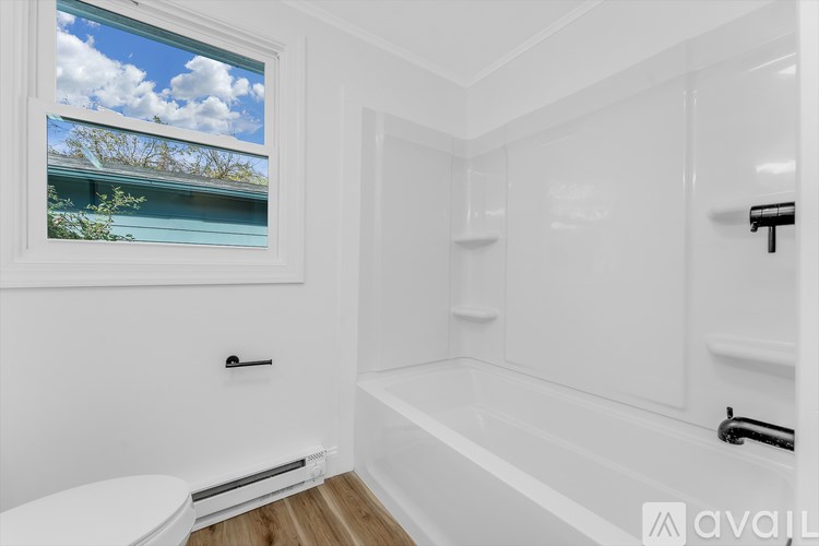 A white bathroom with a window showing a blue sky and trees.
