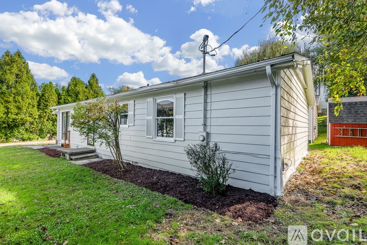 A small white house with a window and a door is surrounded by a grassy area.