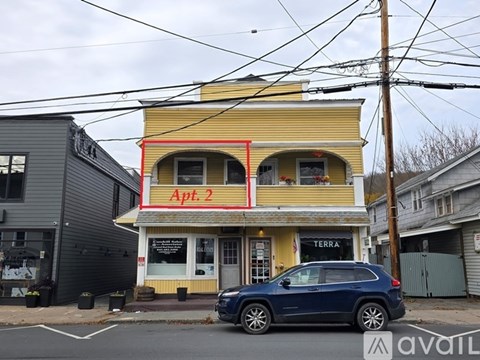 A blue car is parked in front of a yellow building with a sign that reads "Apt. 2".