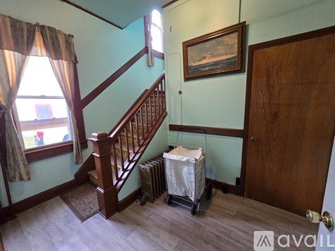 A room with a staircase, a window with curtains, a painting on the wall, and a door.