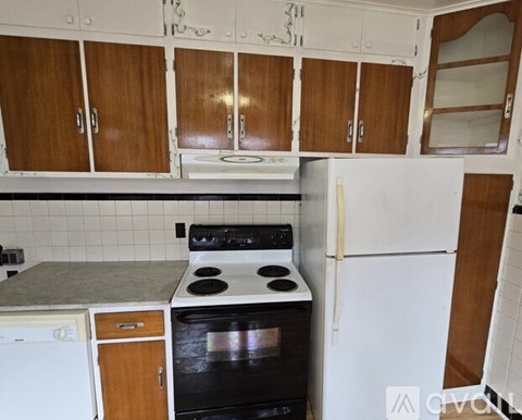 A kitchen with a white fridge, black stove and wooden cabinets.