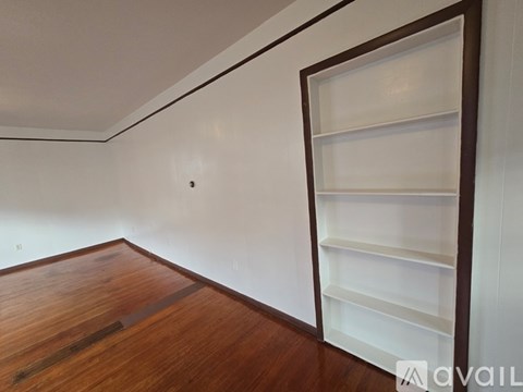 A room with a wooden floor and a white wall with a shelf on the right side.