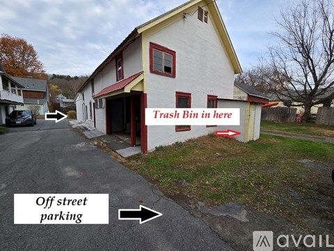 A white building with a red roof and a sign that says "Trash Bin in here" is shown.