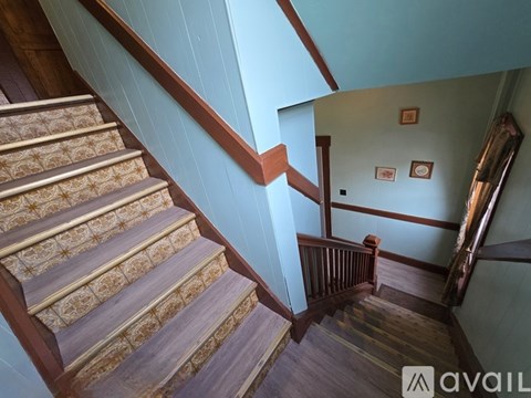 A staircase with a wooden handrail and patterned treads leads up to a landing with a door and two pictures on the wall.