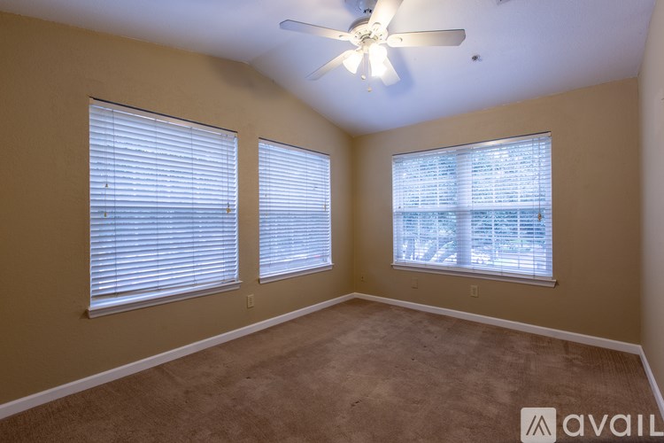 A room with a carpeted floor, a ceiling fan, and two windows with blinds.