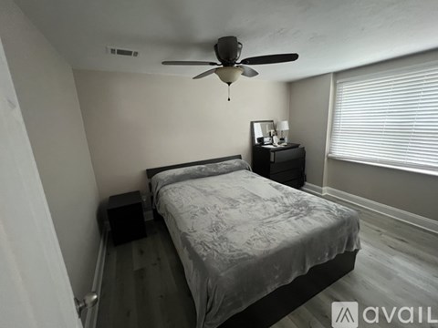 A bedroom with a bed, a ceiling fan, and a nightstand with a lamp.
