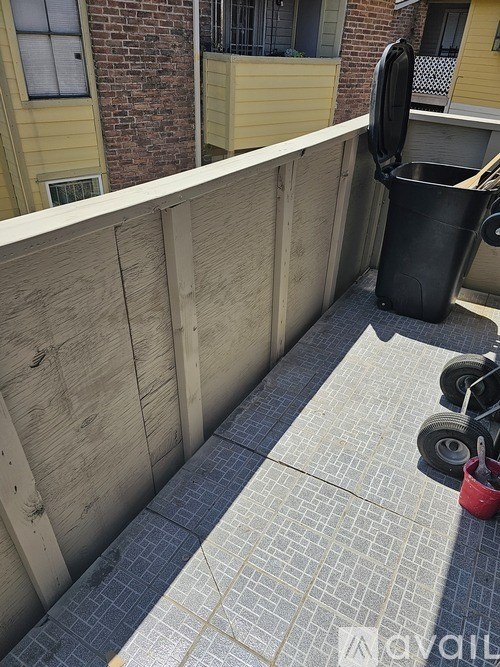 A black trash can is on a balcony with a wooden fence.