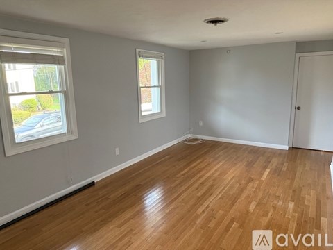A room with wooden flooring and two windows.