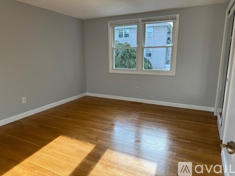 A room with wooden flooring and a window showing a view of a house.