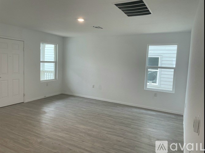 A spacious room with wooden flooring and two windows.