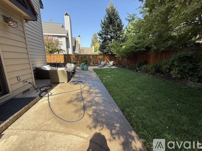 A backyard with a concrete walkway, a fence, and a tree.