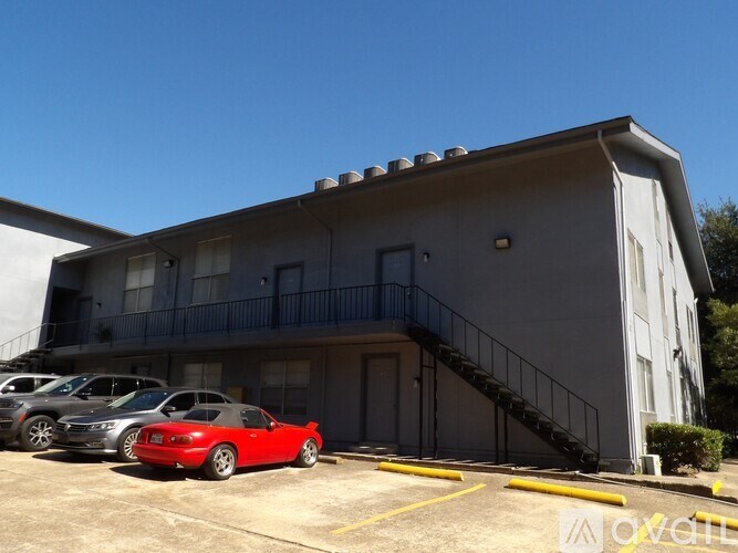A red car is parked in a parking lot in front of a building.